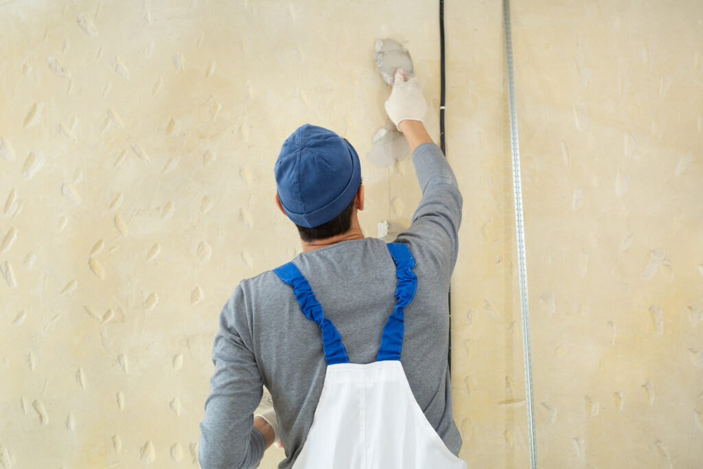 A worker seen from behind adding putty to a wall with a spatula