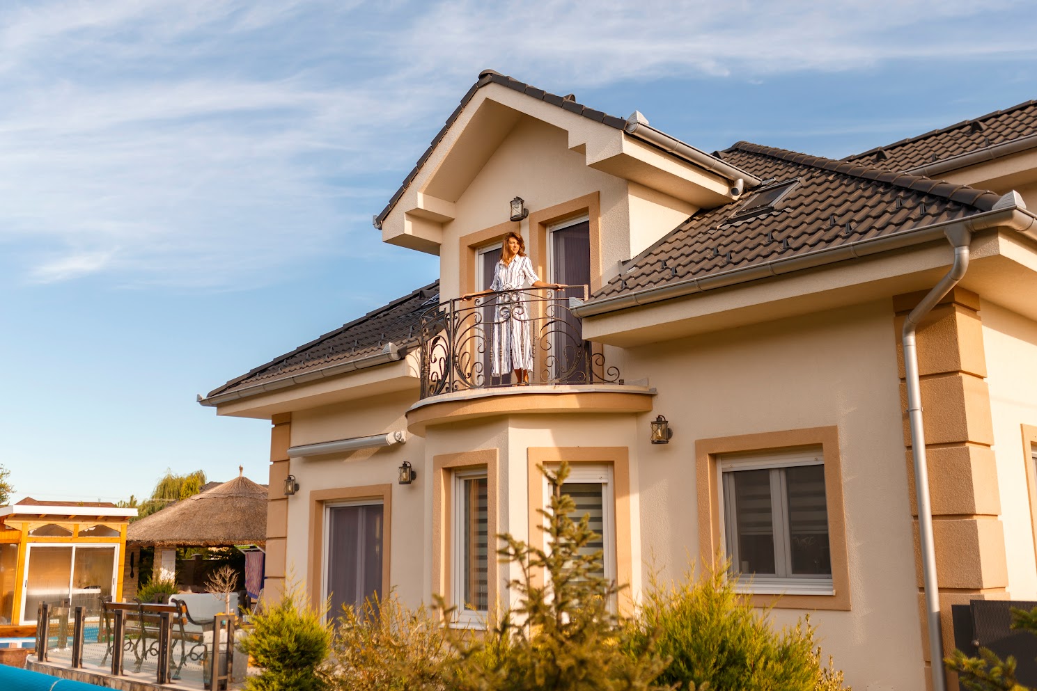 Beautiful young woman standing on her new house balcony happy after purchasing new property